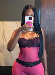 A stylish outfit named 'Very Cutesy Set,' featuring a matching pink two-piece with a mesh design and lace accents. The model is wearing a small size, showcasing the form-fitting set, which includes a pink corset-style top with black lace detailing and matching pink pants. The look is paired with black pointed-toe heels adorned with a rhinestone embellishment, and a small studded black handbag. The model poses confidently on a city street at night, standing in front of a black vehicle.