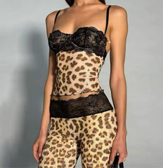 A stylish outfit named 'Very Cutesy Set,' featuring a matching pink two-piece with a mesh design and lace accents. The model is wearing a small size, showcasing the form-fitting set, which includes a pink corset-style top with black lace detailing and matching pink pants. The look is paired with black pointed-toe heels adorned with a rhinestone embellishment, and a small studded black handbag. The model poses confidently 